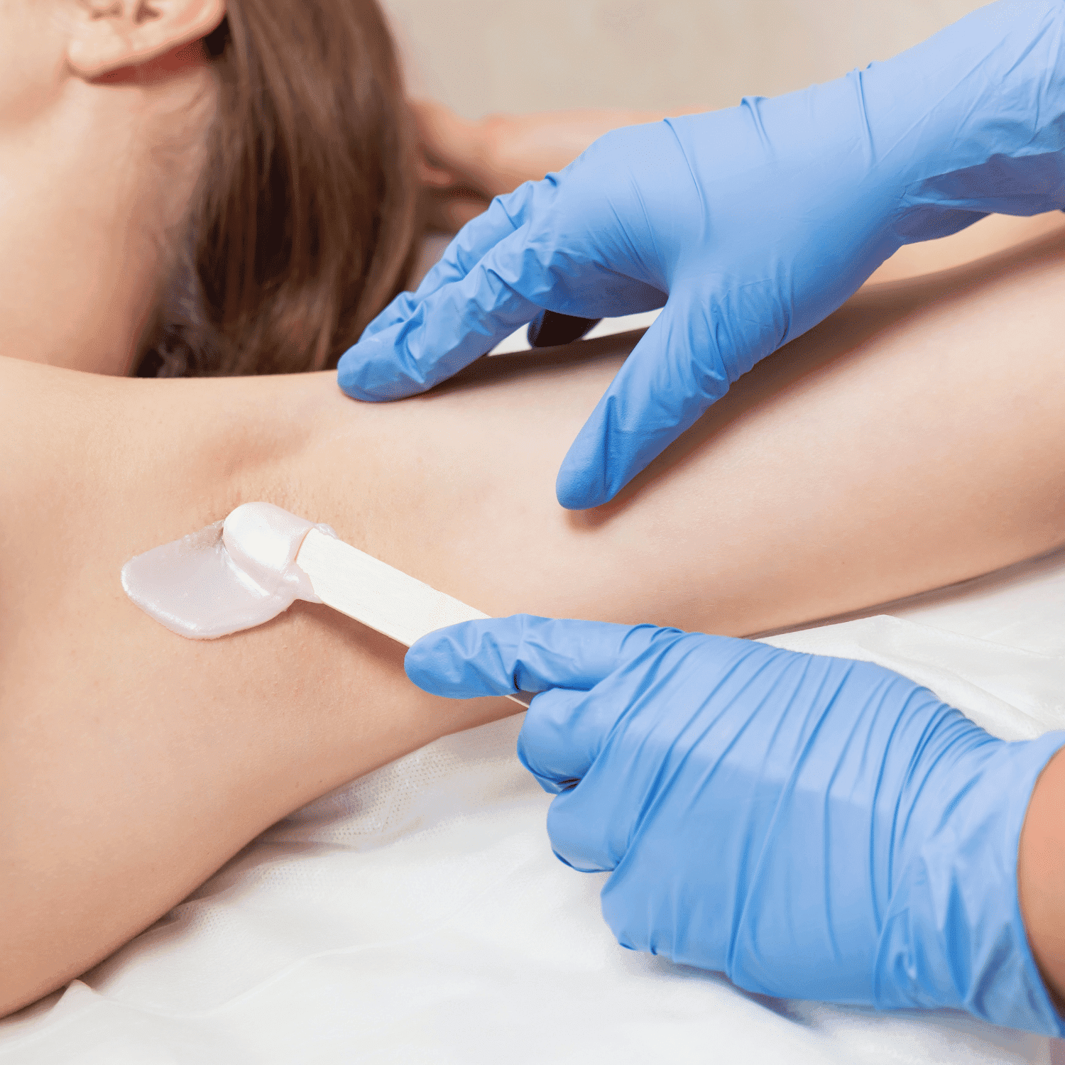 Woman receiving underarm waxing by beautician in blue gloves.