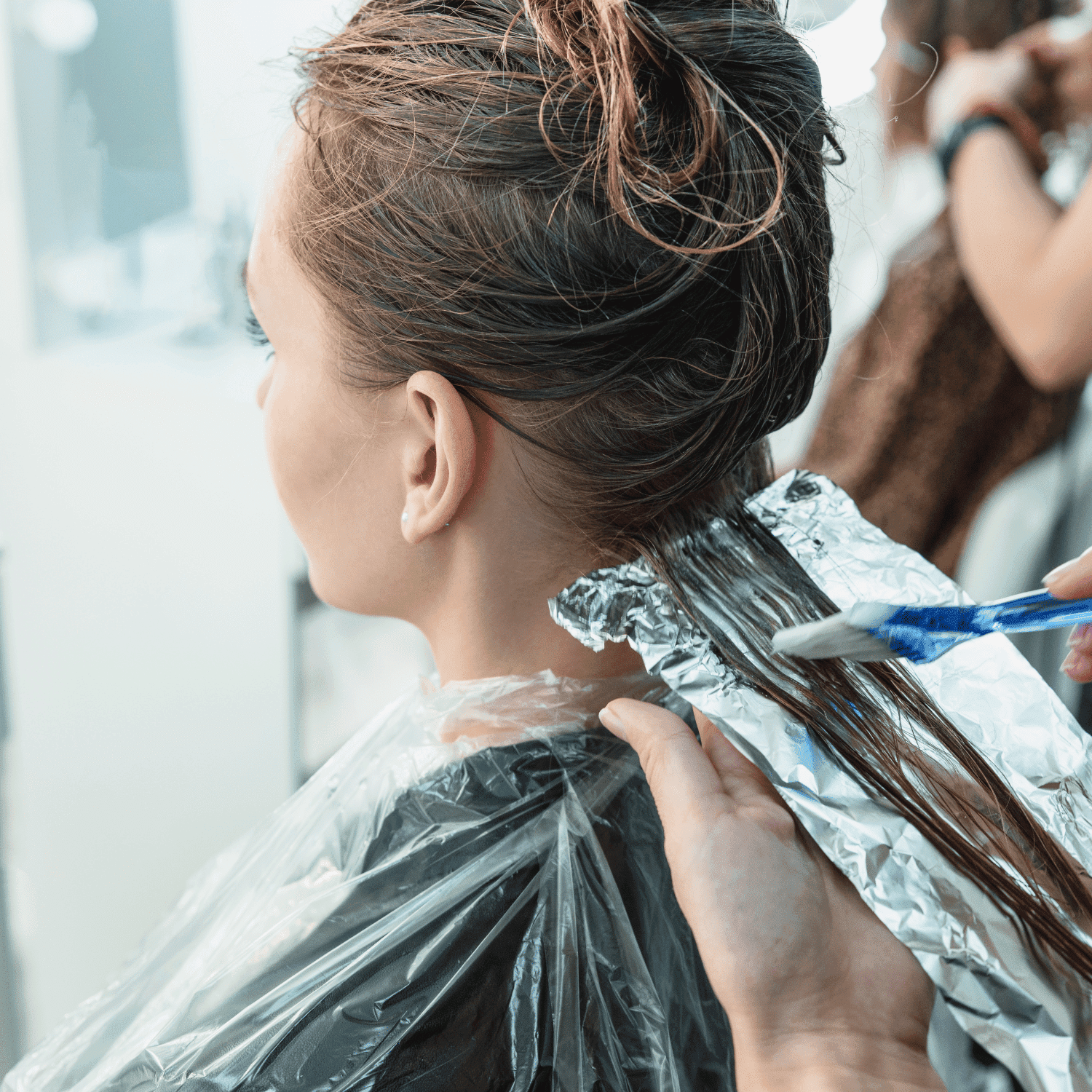 Hairdresser applying color dye to woman's hair at salon.